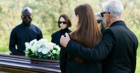Uitvaart; mensen staan om een kist met bloemen